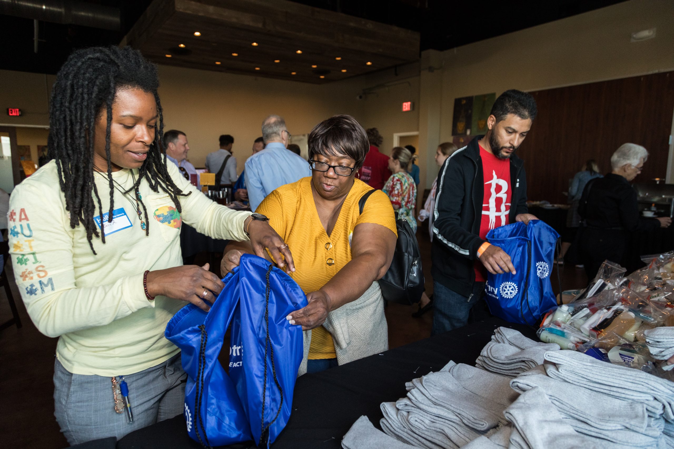 Focused on three people standing in a crowded room at a merch table.