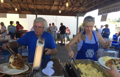 Two people serve eggs and pancakes wearing Rotary Service clothes